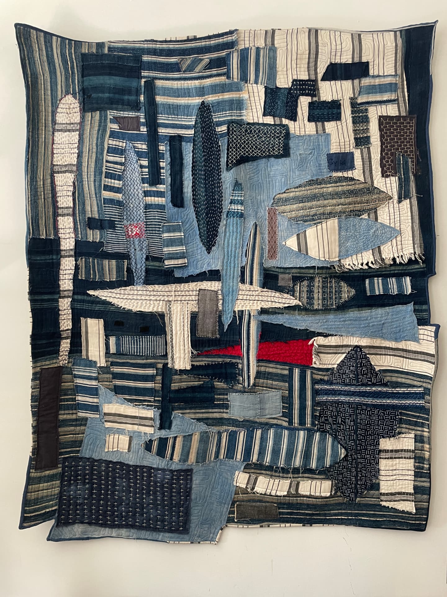Indigo and cream patchwork wall hanging with sashiko stitching and a flash of red