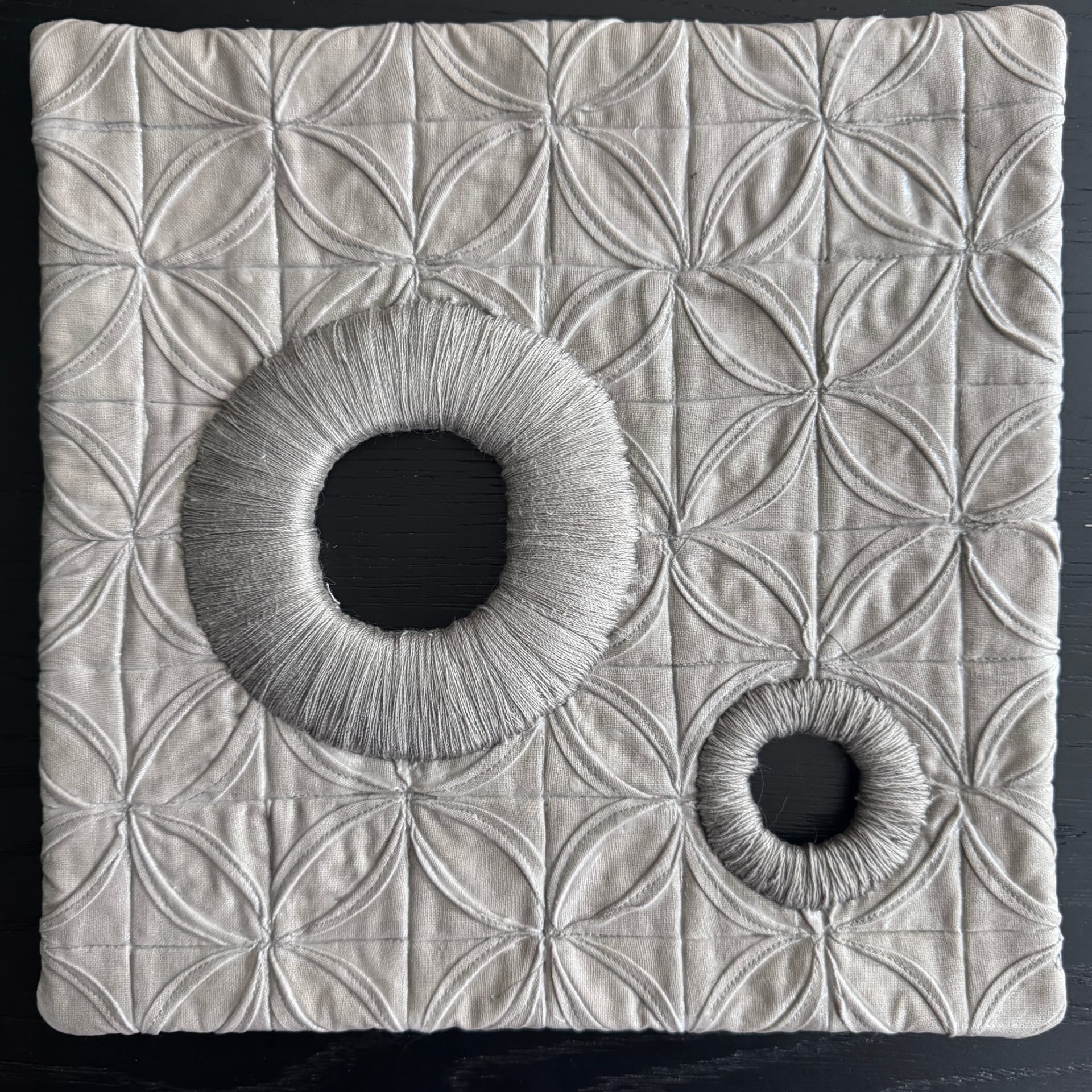 Pale quilted wall hanging with a curved grid and two thread-wrapped circles