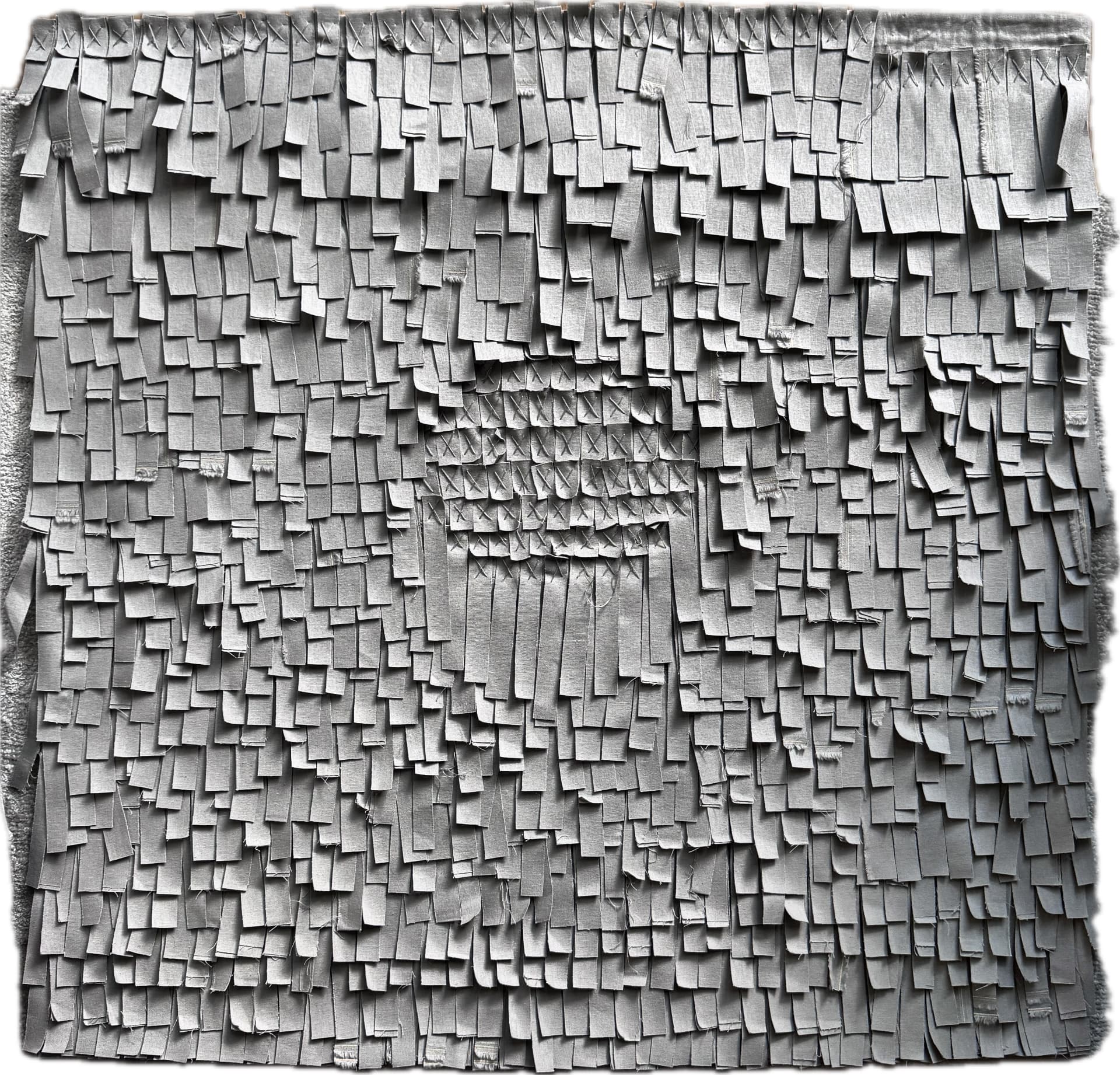 Grey wall hanging made of hundreds of layered, cross-stitched fabric strips