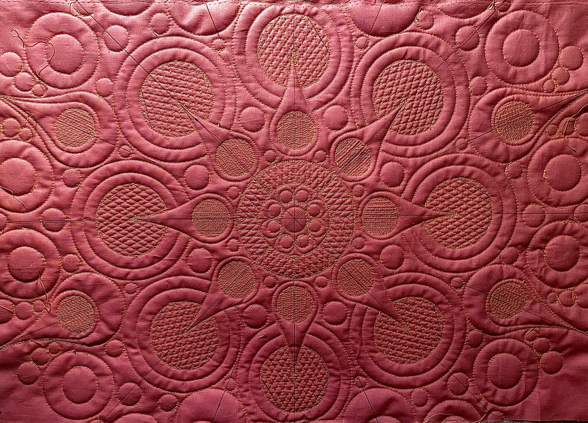 Dusty pink whole-cloth quilt with a radiating medallion of ruler-work circles and fine fill stitching