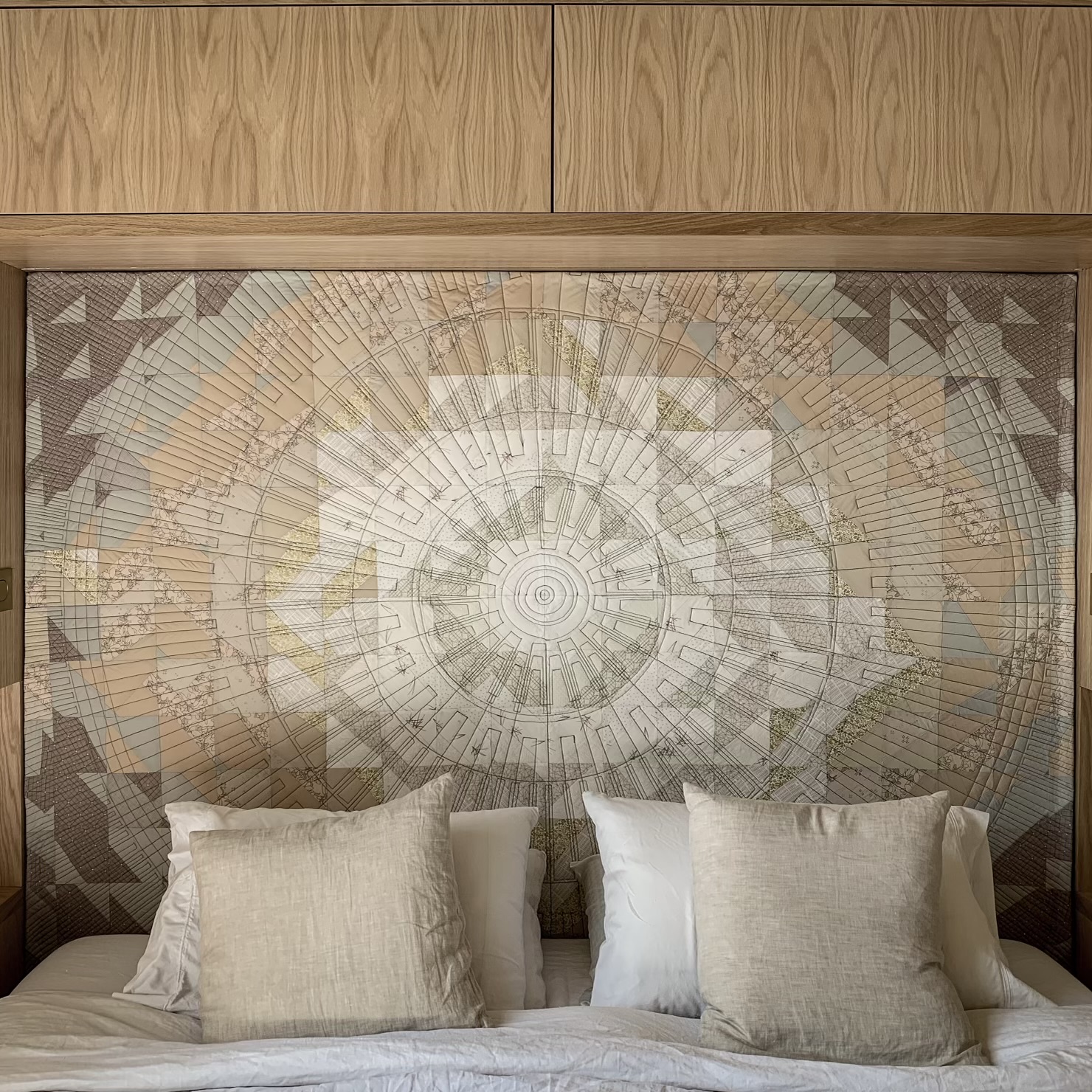 The finished Shimmering Headboard quilt hanging above a bed