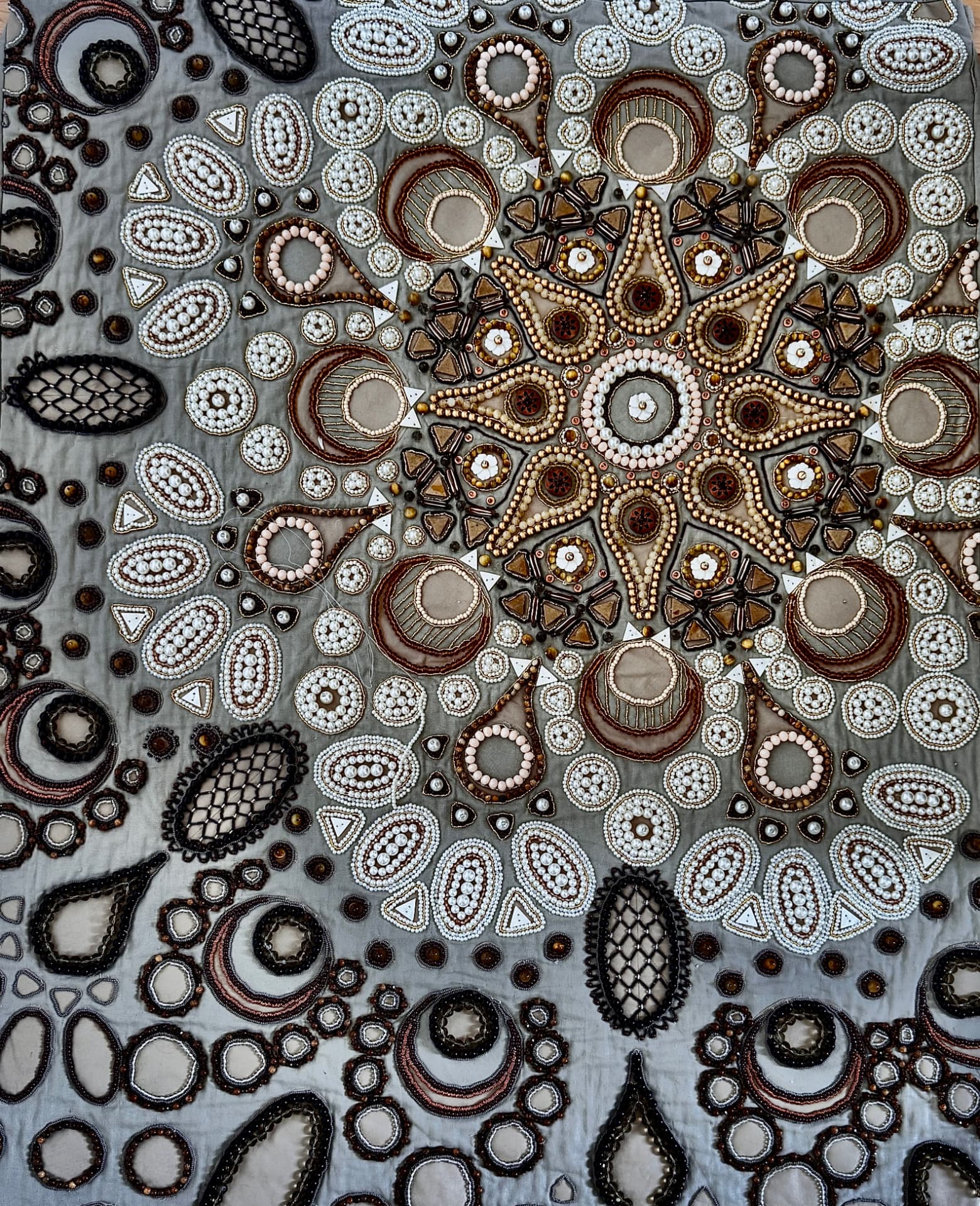 Grey cloth densely beaded with pearls, wood and bronze beads in a radiating medallion